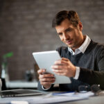 Happy entrepreneur using digital tablet and reading something while working in the office.